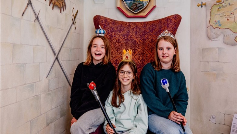 Märchenhotel Waldpension Nebelstein, © Waldviertel Tourismus, Matthias Streibel Drei Kinder mit Kronen und Zeptern sitzen auf einem Thron in einem märchenhaften Raum.