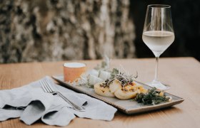 Kartoffelroulade mit Kürbis, Schafkäse und Kräutern gefüllt, © Niederösterreich Werbung/Rita Newman Kartoffelroulade mit Kürbis und Schafkäse auf einem Teller, daneben ein Glas Weißwein.