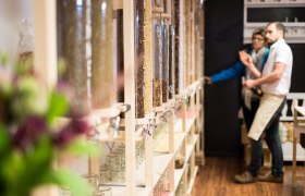 d'Greisslerei in St. Leonhard/Forst, © Jürgen Thoma photography Innenansicht eines Unverpackt-Ladens mit Spendern für lose Lebensmittel und zwei Personen im Hintergrund.