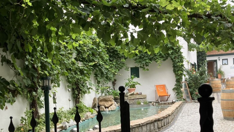 Wunderschöner Innenhof, © Weingut Ruttenstock Ein Innenhof mit Weinreben, einem kleinen Teich und einem Liegestuhl.