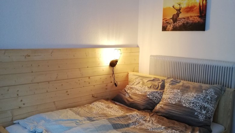 Doppelzimmer, © Familie Weibels Doppelzimmer mit Holzbett und Hirschbild an der Wand.