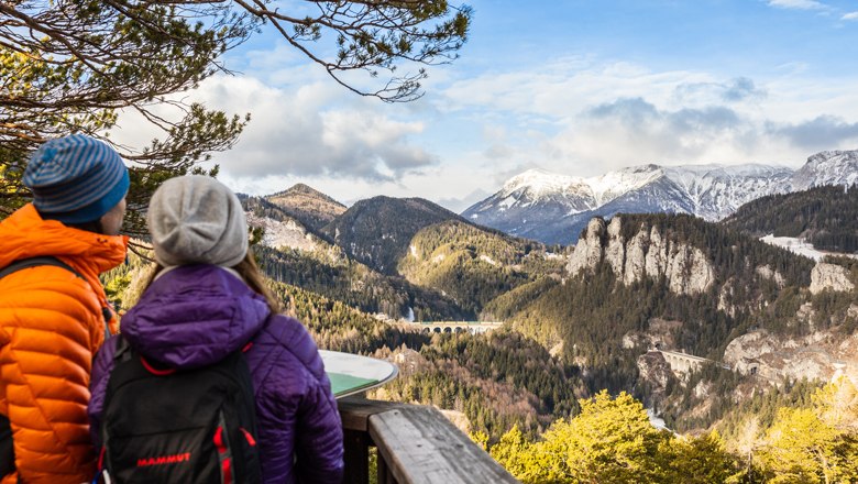 "20-Schilling-Blick" - Wanderung für jede Jahreszeit, © Wiener Alpen - Martin Fueloep Zwei Personen betrachten eine Berglandschaft mit Viadukt.