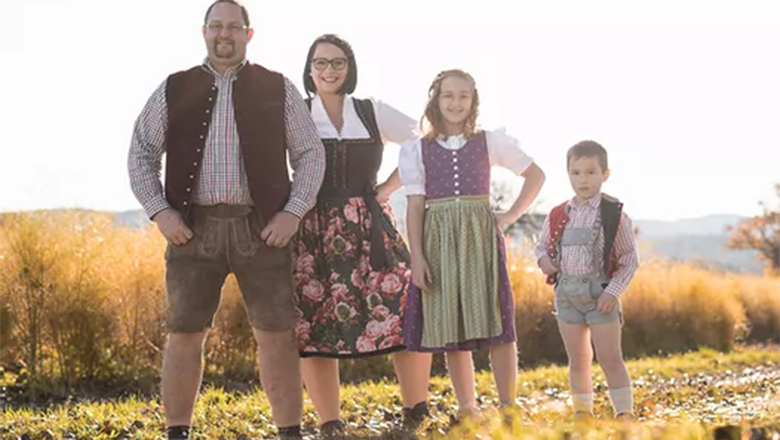 Vitamin Igel´s, © Vitamin Igels Eine Familie mit zwei Kindern in Tracht gekleidet steht auf einem Weg vor einem Feld.