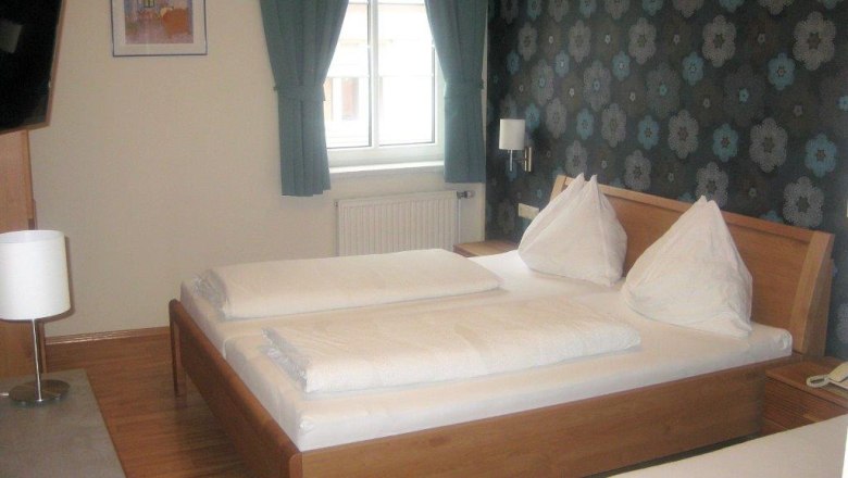 Braugasthof Adlerbrau, Zimmer, © Braugasthof Adlerbräu Hotelzimmer mit Doppelbett, blumiger Tapete und Fenster mit grünen Vorhängen.