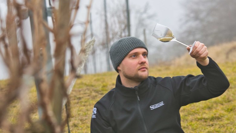 Der Winzer, © Weinbau Stuttner Ein Mann sitzt im Weinberg und betrachtet ein Glas Wein.