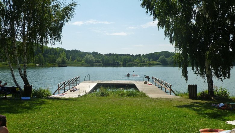 Bergwerksee Langau, © Gemeinde Langau Ein Steg am Bergwerksee Langau mit Menschen, die schwimmen und sich sonnen. Umgeben von Bäumen und grüner Wiese.
