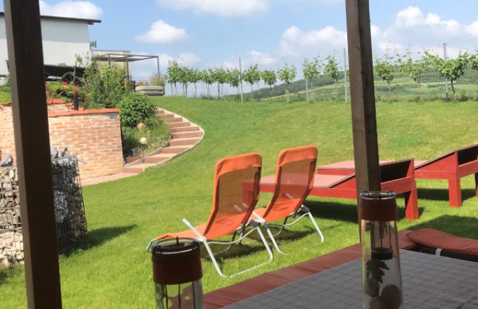 Terrasse, © Reinhard Gurschka Blick von einer Terrasse auf einen Garten mit Liegestühlen und Weinreben im Hintergrund.