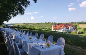 Tafeln im Weinviertel, © Weinviertel Tourismus GmbH Lange Tafel im Freien mit weißer Tischdecke, gedeckt für ein Festessen, im Hintergrund ein Gebäude und grüne Felder.