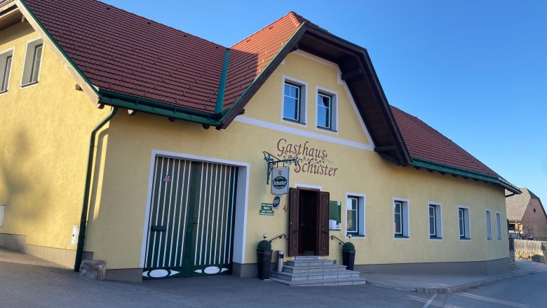 Gasthaus Schuster, © Wiener Alpen Gelbes Gebäude mit rotem Dach, beschriftet als Gasthaus Schuster.