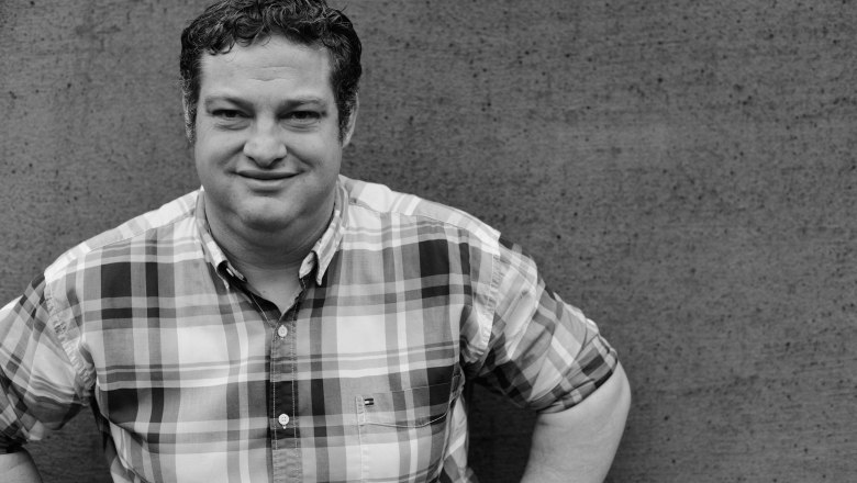 Christian Edelmann, Weingut Edelmann Göttlesbrunn, © Die Rubin Carnuntum Weingüter Schwarz-weiß Foto eines Mannes in kariertem Hemd vor einer Betonwand.