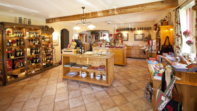 Mohnshop, © Waldviertler Mohnhof Innenansicht eines gemütlichen Ladens mit Holzregalen, die Weinflaschen und andere Produkte präsentieren. Dekorationen mit Mohnblumen sind sichtbar.