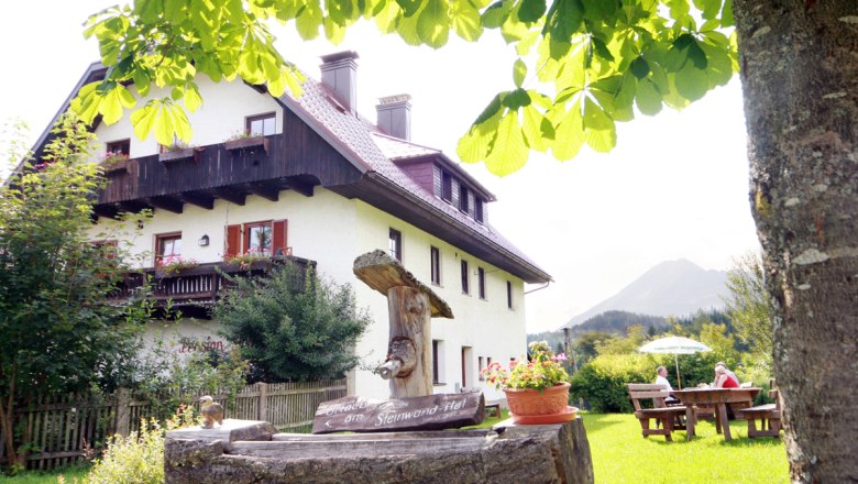 Steinwandhof, © weinfranz.at Ein traditionelles Bauernhaus mit Holzbalkon, umgeben von grüner Natur und einem Baum im Vordergrund.