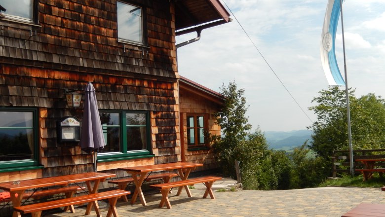 Kaiserkogel Hüte, © ÖTK Eschenau Holzhütte mit Terrasse und Bänken, Flagge weht im Wind.