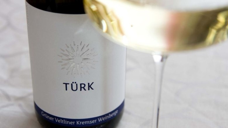 tuerk-2, © Weingut Türk Weinflasche mit Etikett 'TÜRK' und Weinglas mit Weißwein.