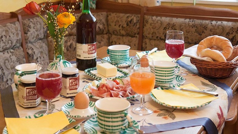Frühstück, © Fam. Wilhelm Ein gedeckter Frühstückstisch mit Brötchen, Marmelade, Eiern, Saft und Blumen.
