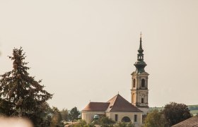 Weinherbst in Niederösterreich, Donau in Niederösterreich, © Niederösterreich Werbung/Discover Austria In der sanften Hügellandschaft blühen die Rosen in voller Pracht und umrahmen die malerische Kirche, die stolz über das Dorf wacht. Die goldenen Strahlen der Sonne tauchen die Szenerie in ein warmes Licht und laden dazu ein, die Schönheit der Natur zu genießen.
