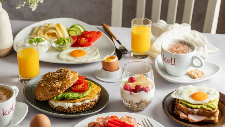 Frühstück bei der Bäckerei Koll, © Michaela Begsteiger, Koll GmbH Frühstückstisch mit Brötchen, Aufschnitt, Spiegelei, Joghurt mit Beeren, Orangensaft und Kaffee.