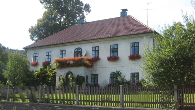 Gsolhofer Dirndlladen, © zVg Ein zweistöckiges Haus mit roten Dachziegeln und Blumenkästen an den Fenstern.