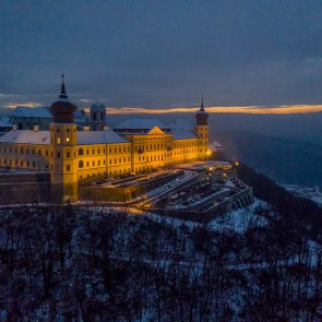 beleuchtetes Schloss bei Nacht auf Hügel mit schneebedeckter Landschaft