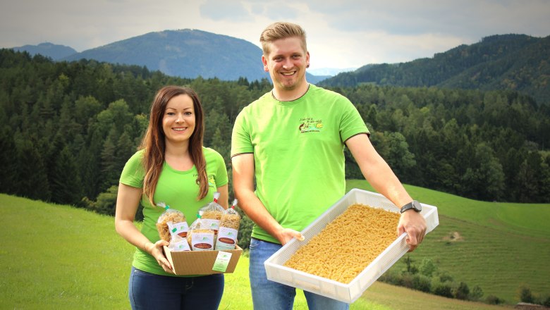Aus der Nudelwerkstatt List, © Familie List Zwei Personen in grünen T-Shirts präsentieren Nudeln vor einer Berglandschaft.