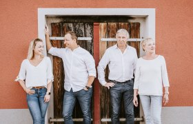 Familie Ladentrog, © Stefan Jurecek Vier Personen stehen vor einer Holztür, alle in weiß gekleidet.