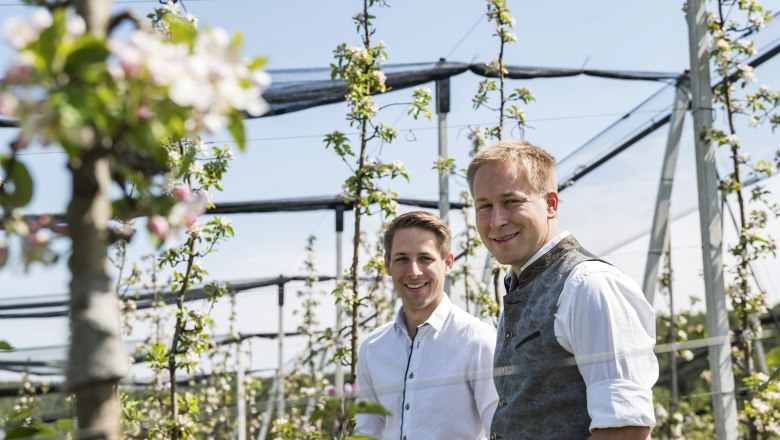 Apfelblüte im Obstgarten vom MostMichl, © Thomas Gobauer-Photography Zwei Männer stehen in einem blühenden Apfelgarten.