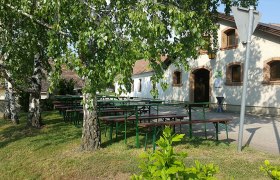 Heuriger Fam. Ernst Fröschl, © Fam. Fröschl Außenbereich eines Heurigen mit Biertischen unter Bäumen.