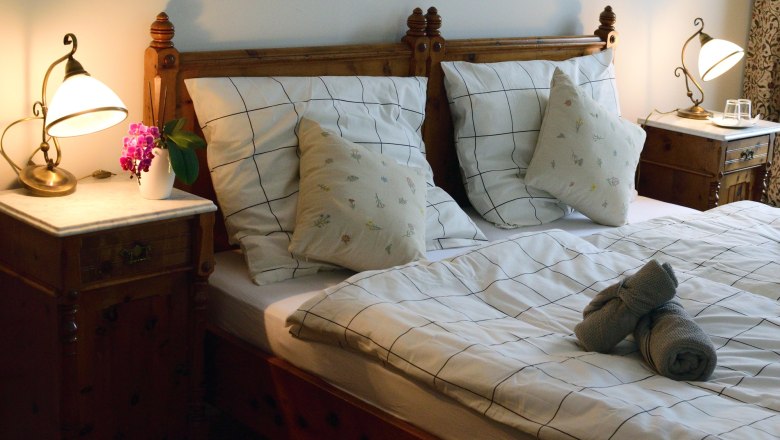 Doppelzimmer, © Reinhard Maurer Gemütliches Doppelzimmer mit Holzmöbeln, Bett mit kariertem Bettzeug, Nachttischen und Lampen.