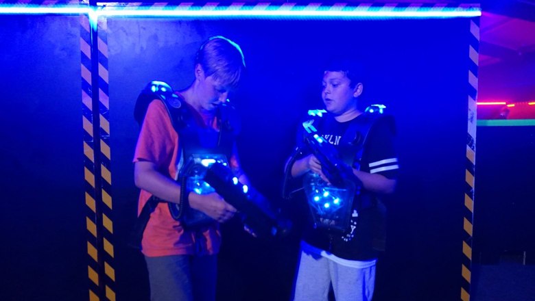 Laser Tag zu zweit, © Suracon OG Zwei Jungen in einer Laser-Tag-Arena mit leuchtenden Westen und Laserpistolen.