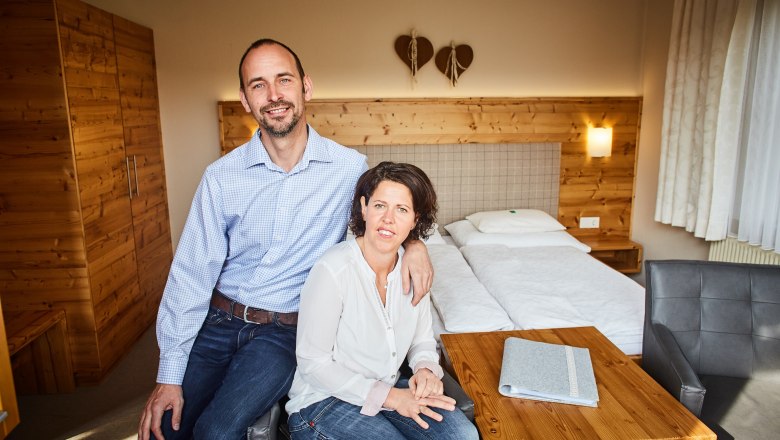 Zimmer am Bauernhof Dissauer Familie Rosinger, © Familie Rosinger Ein Paar sitzt in einem gemütlichen Zimmer mit Holzmöbeln und einem Doppelbett.