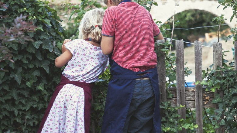 Naschkatzen, © Monika Pölzer Zwei Kinder stehen auf einer Bank und schauen über einen Zaun in einen Garten.