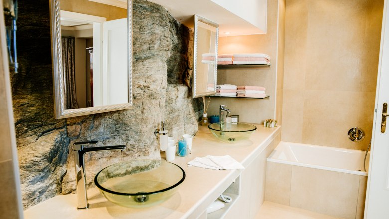 villa_schonthal-21_3, © Julius Hirtzberger Modernes Badezimmer mit Glaswaschbecken und Natursteinwand.