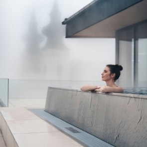 Wellness im Winter, © Niederösterreich Werbung/Ian Ehm Frau entspannt in einem Infinity-Außenpool, im Hintergrund Nebel und Kirchentürme