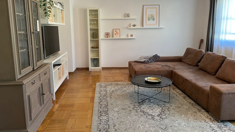 Ferienhaus Stixneusiedl, Wohnzimmer, © Karoline Wolfger Wohnzimmer mit braunem Sofa, Teppich, Kronleuchter und TV-Schrank.