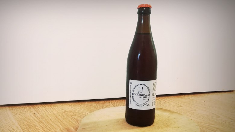 Weizenbier vom Holzbräu, © Wiener Alpen Eine Flasche Weizenbier vom Holzbräu steht auf einem runden Holzbrett mit Griff.