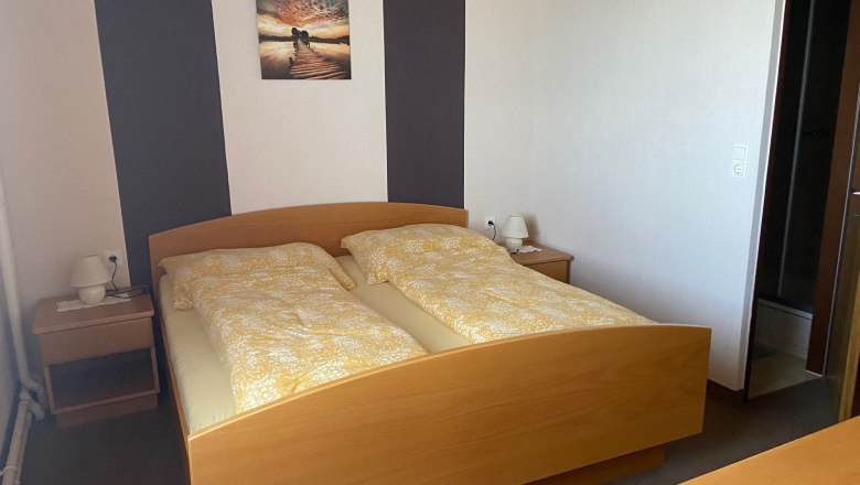 Doppelzimmer, © Wiener Alpen Ein Doppelzimmer mit einem Holzbett, zwei Nachttischen und einem Bild an der Wand.