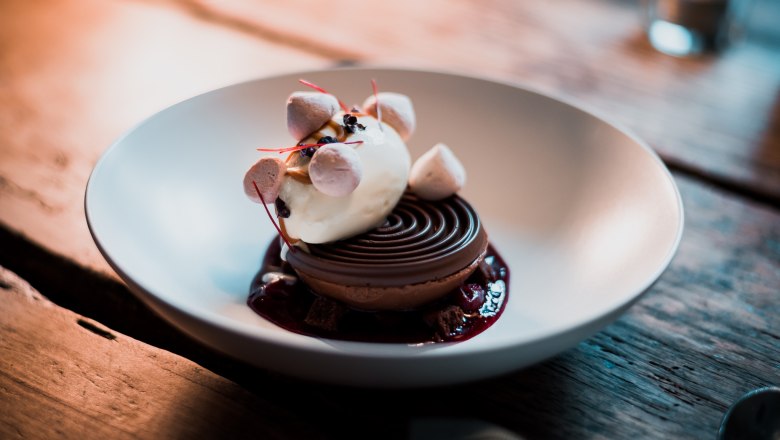 Schokoladen Kuppel - Mousse / Brownie / Eis / Crumble, © Vinzenz Pauli/Philip Hinteregger Ein Dessert mit Eis, Mousse und Crumble in einer Schale serviert.