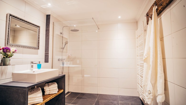 Roth_2Bad, © Georg Pomassl Modernes Badezimmer mit großer Dusche, Waschbecken, Spiegel und Handtüchern.