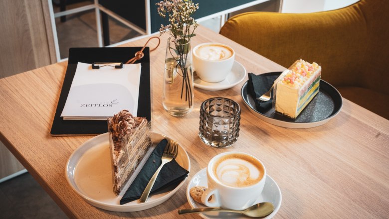 TDR- ZEITLOS-Torten, © Philipp Elsler Café-Tisch mit zwei Kuchen und Cafés mit Speisekarte und Blume.