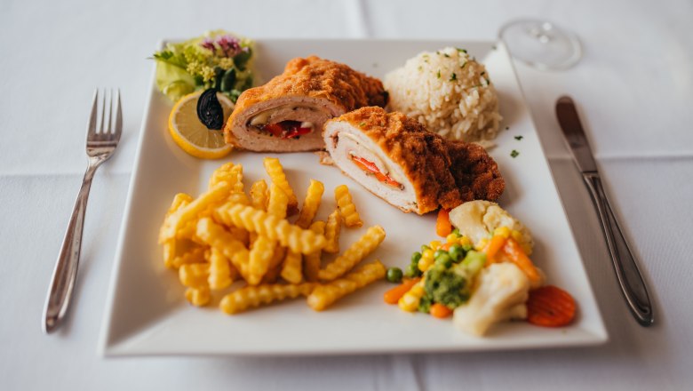 Nussendorfer Hochzeitsschnitzel, © Niederösterreich Werbung/Daniela Führer Gebackenes Hähnchen mit Pommes, Reis und Gemüse auf weißem Teller.