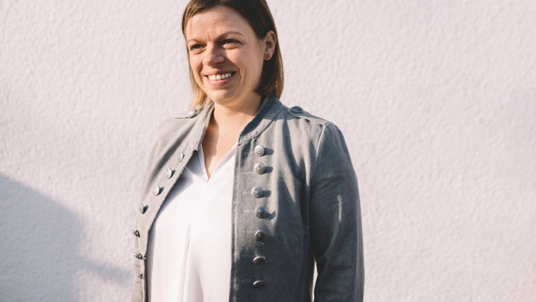 Im Service: Sandra Buchinger-Löfler, © Niederösterreich Werbung/Mara Hohla Frau in grauer Jacke vor weißer Wand.