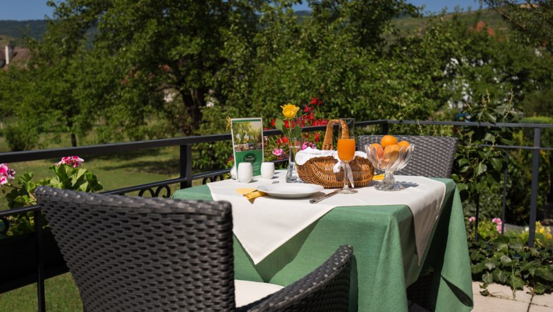 Terrasse, © Donauhof/ Marcel Musiol Ein gedeckter Tisch auf einer Terrasse mit grünem Tischtuch, Saft, Obst und Blumen, umgeben von grüner Natur.