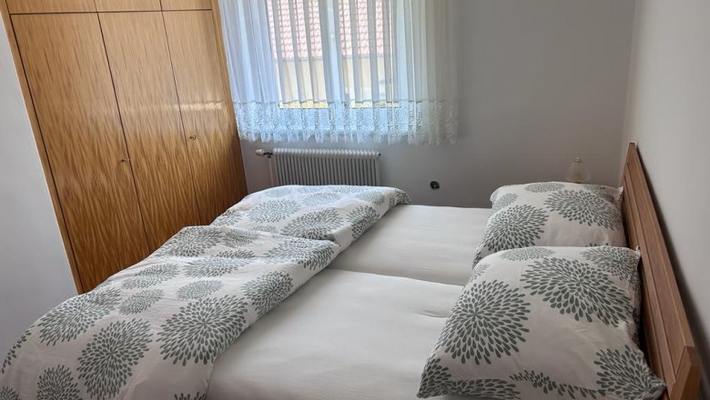 Schlafzimmer, © Kainz-Waldinger Ein Schlafzimmer mit einem Doppelbett, weißen Vorhängen und einem Holzkleiderschrank.