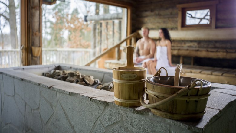 Hotel Sole Felsen Welt, © Waldviertel Tourismus, Robert Herbst Innenansicht einer Sauna mit zwei Personen im Hintergrund, die auf Holzbänken sitzen. Im Vordergrund sind Saunaeimer und Steine zu sehen.
