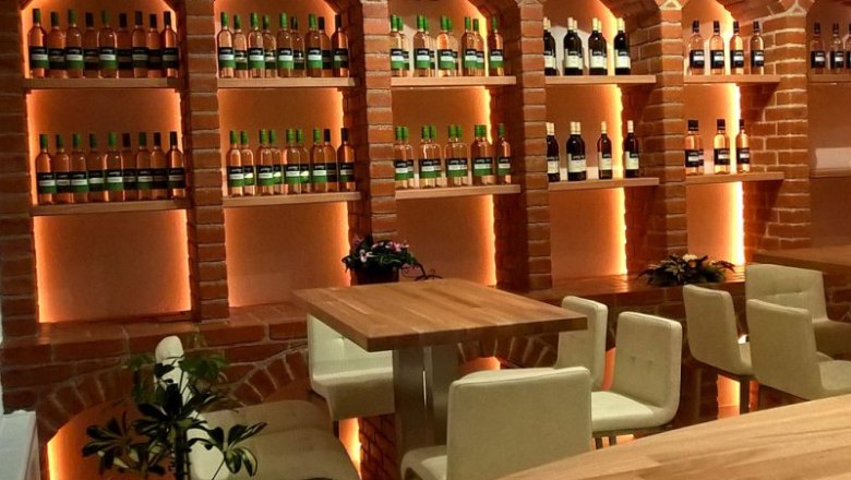 pichler_verkostlokal, © Weinbau Pichler Gemütliches Verkostungslokal mit Ziegelregalen voller Weinflaschen und Holztischen.