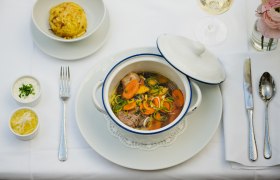 Herzlich Willkommen, © NÖ Werbung / Martina Siebenhandl Ein gedeckter Tisch mit einem Eintopf in einem weißen Topf, einem Knödel, zwei Soßen und einem Glas Weißwein.