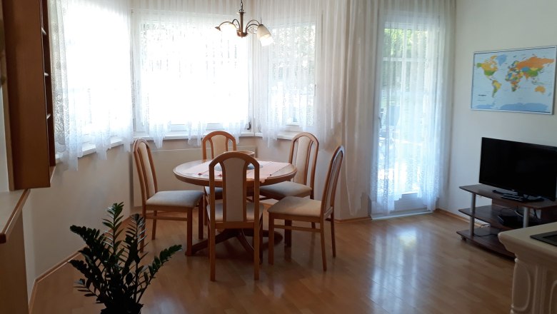 Wohnküche, © Barbara Muck Helle Wohnküche mit Esstisch, Stühlen, TV und Weltkarte an der Wand.