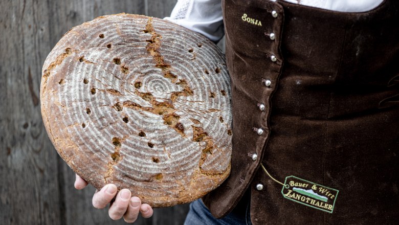 Frisches selbstgebackenes Brot, © Martina Siebenhandl Person hält rundes, selbstgebackenes Brot vor rustikalem Hintergrund.