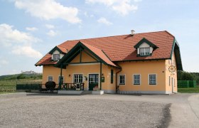 Aussenansicht Severinhof, © Familie Schwaighofer Ein gelbes Gebäude mit rotem Dach und grünen Akzenten, umgeben von einer ländlichen Landschaft.