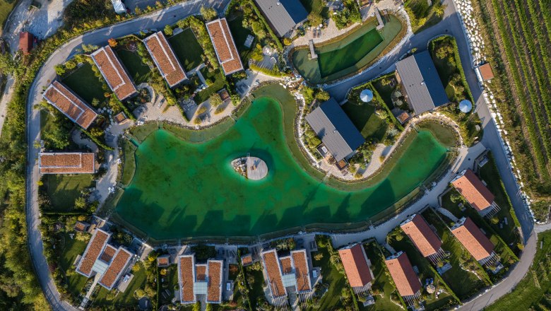 Kittenberger Chalets am Gartensee, © Niederösterreich Werbung / Maximilian Pawlikowsky Luftaufnahme von Chalets um einen grünen See mit Steg in der Mitte.